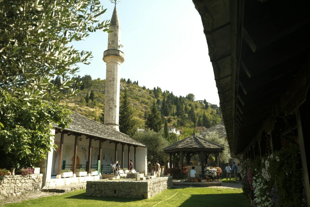 Beautiful mosque courtyard in Stolač, Bosnia surrounded by greenery under a clear blue sky.