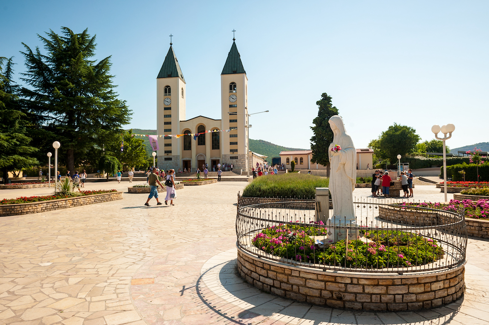 Medjugorje Sanctuary in Bosnia and Herzegovina. In the foreground is the vigin Mary statue and in the background is the parish church.