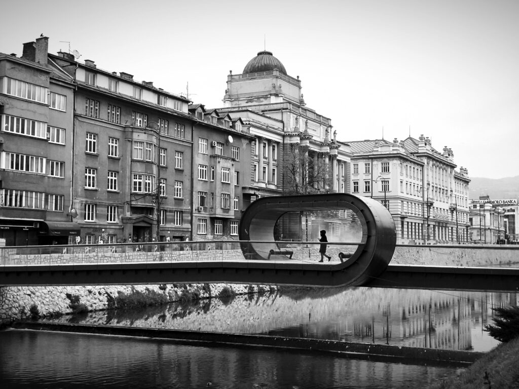 pexels-photo-29450686-29450686 A monochrome image capturing the modern Festina Lente bridge in Sarajevo with historic buildings.