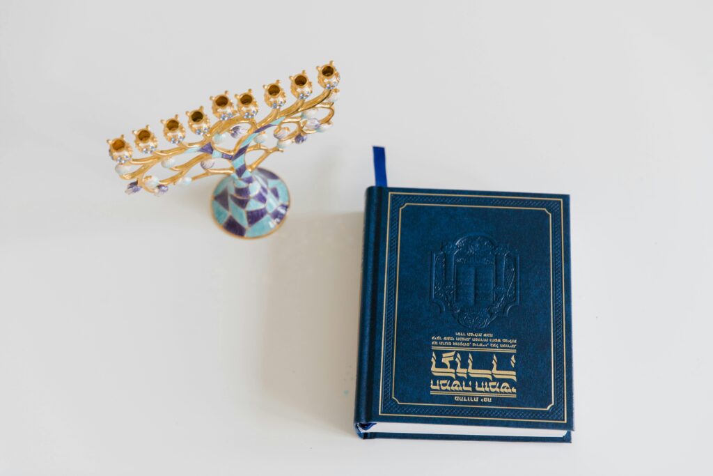 pexels-photo-9242403-9242403 An ornate menorah and a Hebrew book on a white surface, perfect for Hanukkah themes.