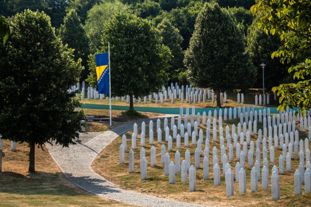 pexels-photo-32933054-32933054 A solemn view of the Srebrenica Memorial, featuring rows of white gravestones and the Bosnian flag.